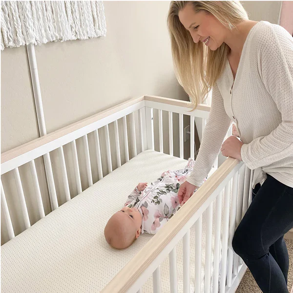 Woman leaning over a white crib toward a baby lying on a crib mattress