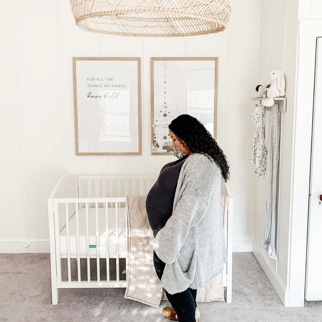 Pregnant person standing beside a white crib in a bright nursery