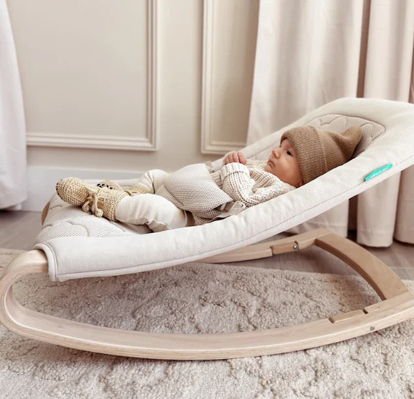 Baby lying in a cushioned rocker with a light wood frame on a rug.
