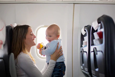Woman holding a smiling baby beside an airplane window with seats visible around them