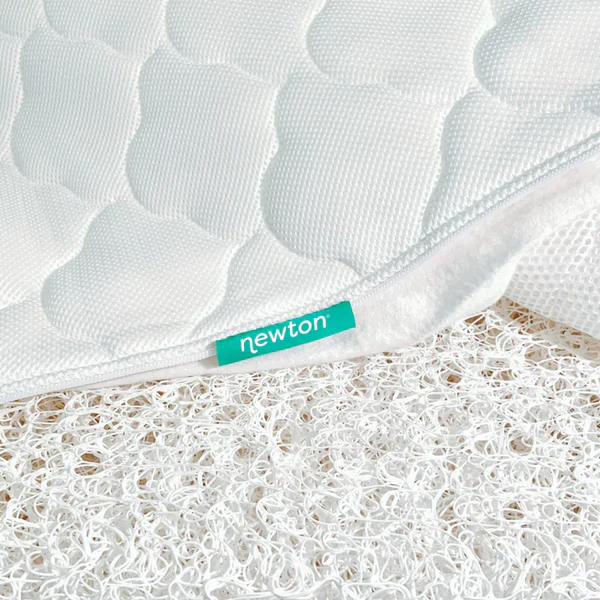 Close-up of a white quilted mattress cover with a teal tag reading "newton" above a white mesh layer.