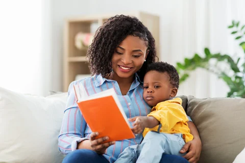 Adult and young child sitting on a sofa while looking at an orange book