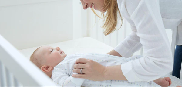 Adult leaning over a baby lying on their back in a white crib.