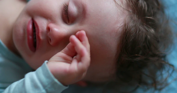 Sleeping baby in a light blue top with one hand resting near their face