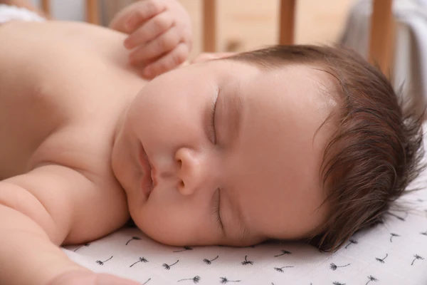 Sleeping baby resting on a patterned sheet with eyes closed