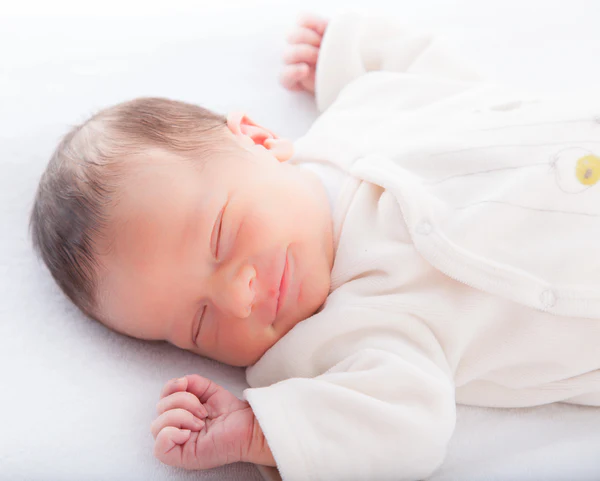 Sleeping baby in a white outfit lying on a light surface