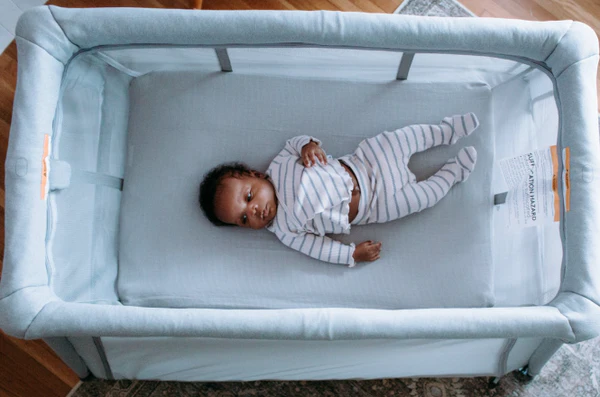 Baby lying on their back in striped pajamas inside a light blue mesh-sided crib