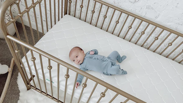 Baby lying on a white crib mattress inside a metal crib with vertical rails.