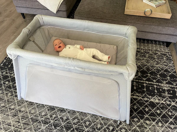 Baby lying on their back in a gray play yard in a living room
