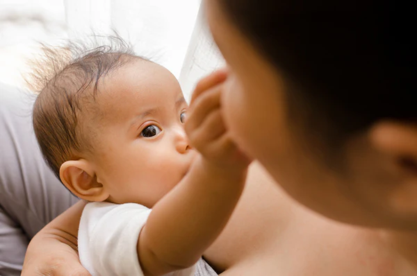 Baby nursing while touching an adult's face in a close-up scene