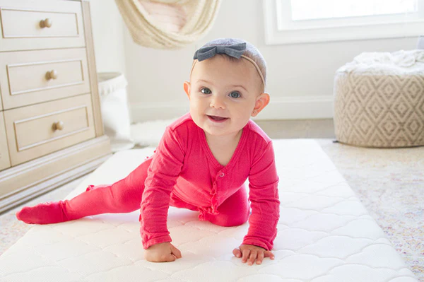 Smiling baby in a pink outfit crawling on a white mat in a bright nursery