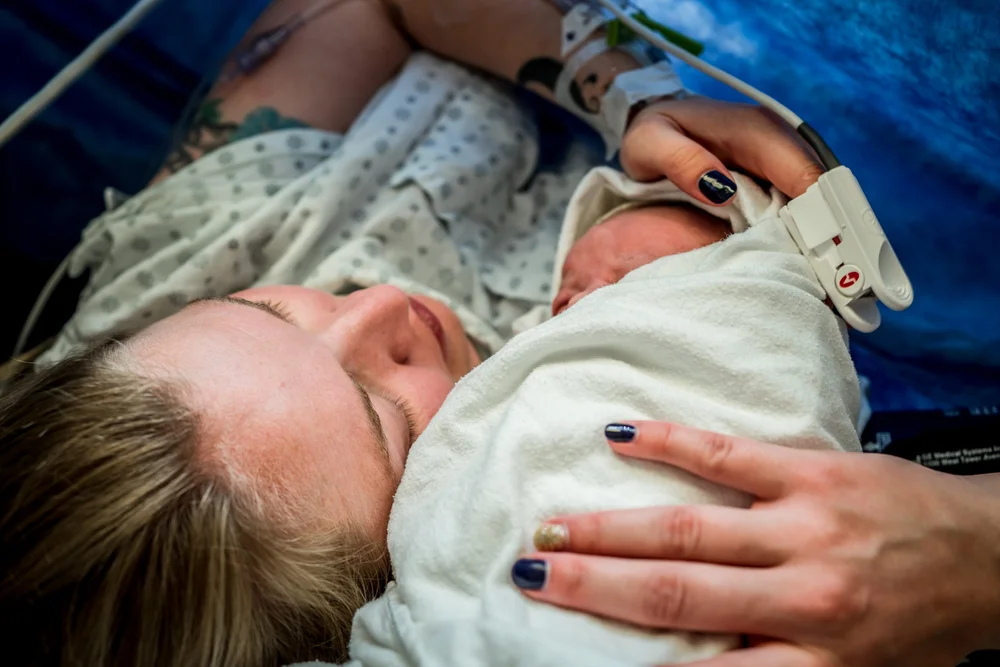 Person in a hospital gown holding a swaddled newborn close against their chest