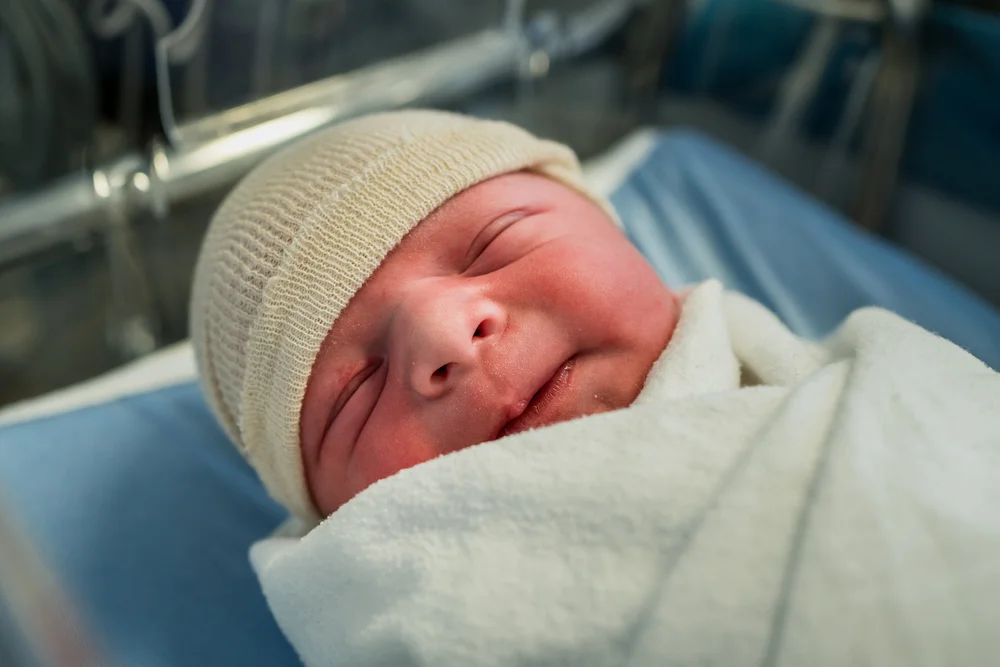 Newborn baby wrapped in a white blanket and wearing a knit cap, lying in a hospital bassinet