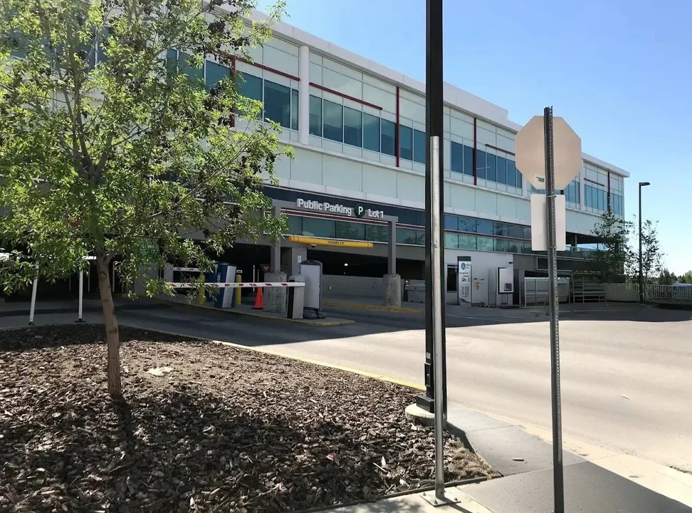 Parking garage entrance with Public Parking P Lot1 sign, gate arms, trees, and street signs.
