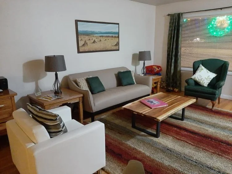 Cozy living room with sofas, armchair, coffee table, lamps, framed wall art, rug, and curtained window