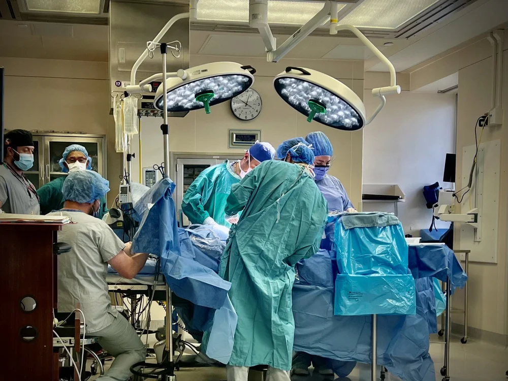 Medical team in surgical gowns gathered around a patient under operating room lights