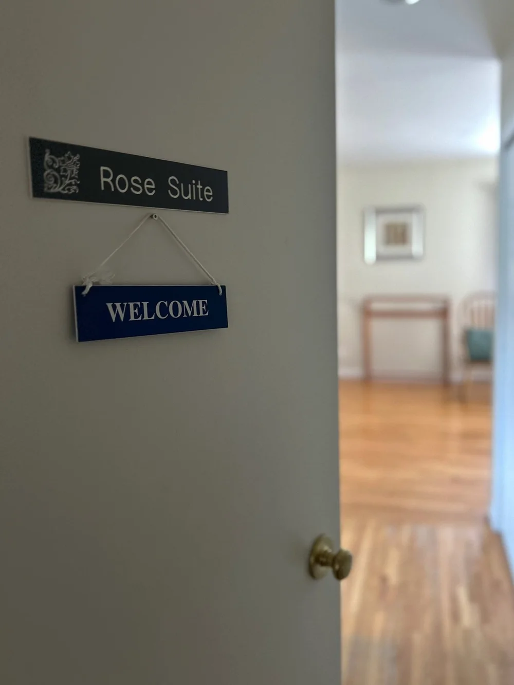 Doorway sign reading Rose Suite above a welcome sign, with a softly blurred room beyond