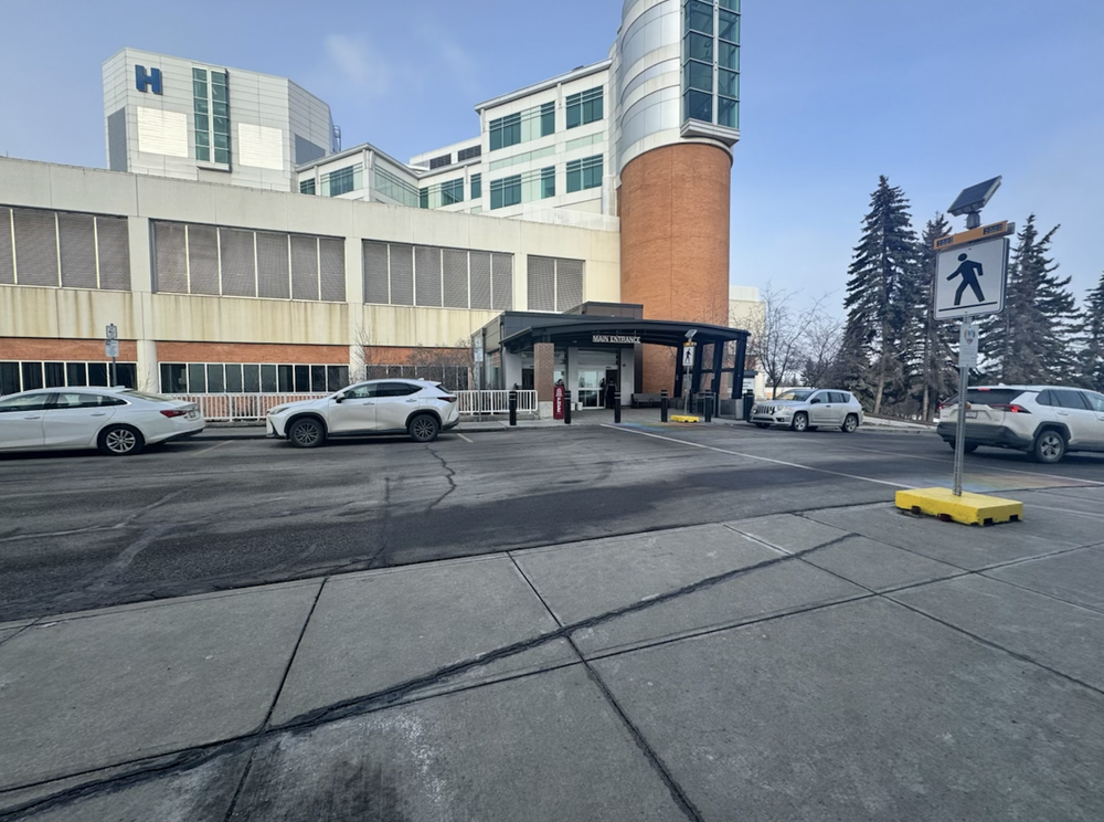 Hospital entrance with parked cars, a crosswalk sign, and multi-storey building facade