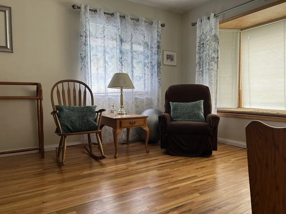 Quiet sitting room with a rocking chair, recliner, lamp, curtained windows, and wood flooring