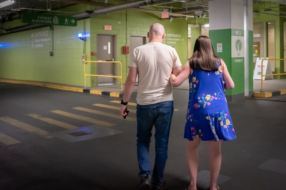 Two people walking through a green hospital parking garage toward entrance signs and elevators