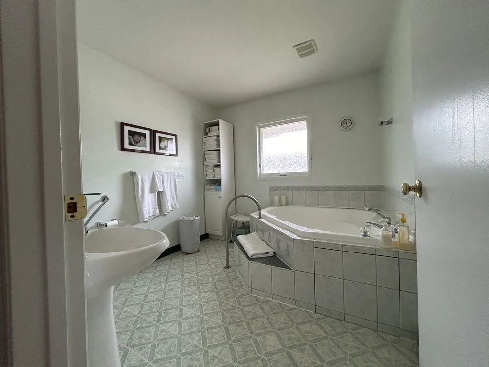 Bathroom with pedestal sink, towel rack, tiled bathtub, frosted window, shelves, and patterned green floor.