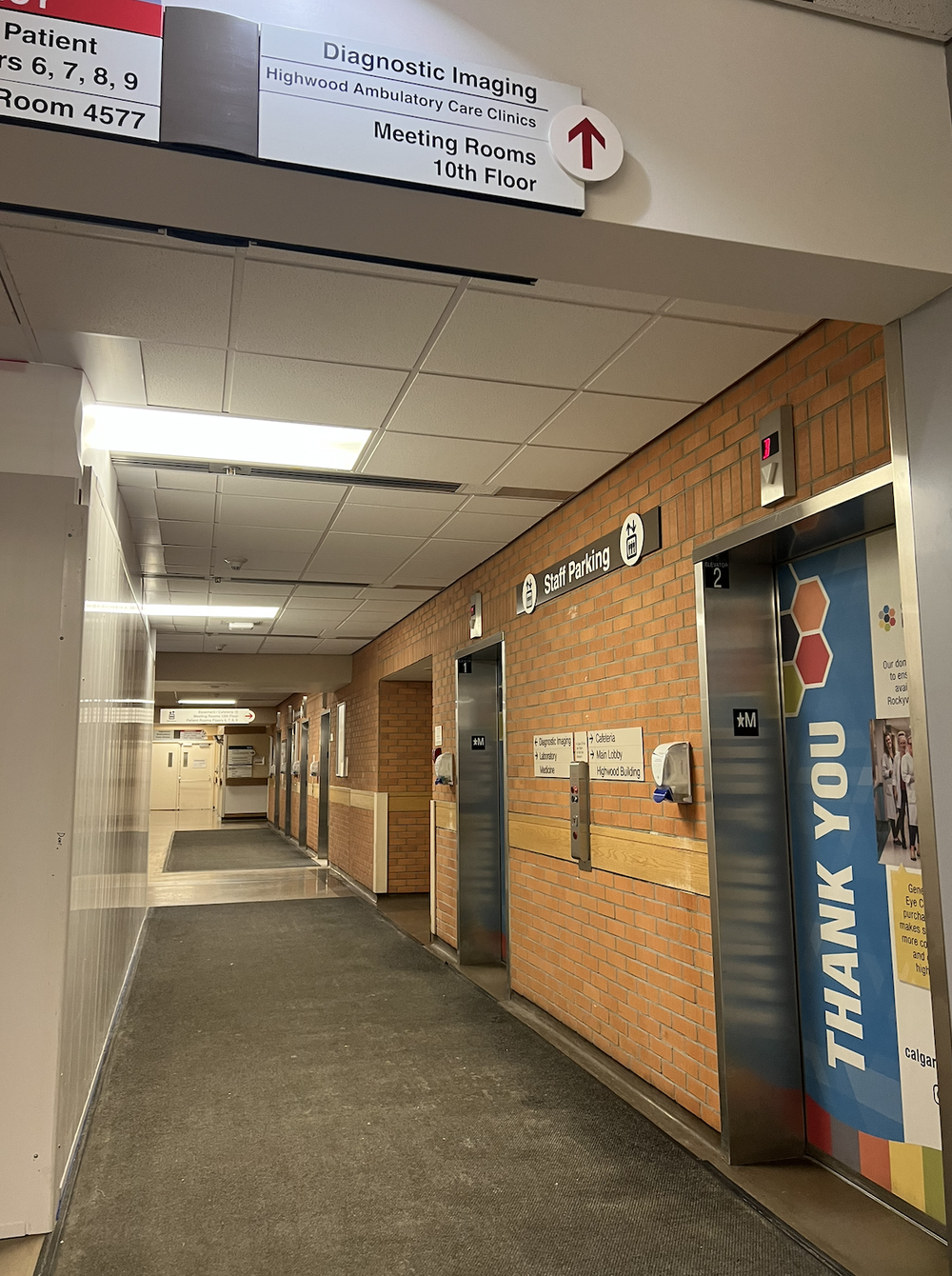 Hospital corridor with elevator banks, brick wall, and signs for Diagnostic Imaging and meeting rooms