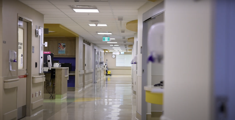 Clean hospital corridor with doors, hand sanitizer dispensers, and overhead exit signs