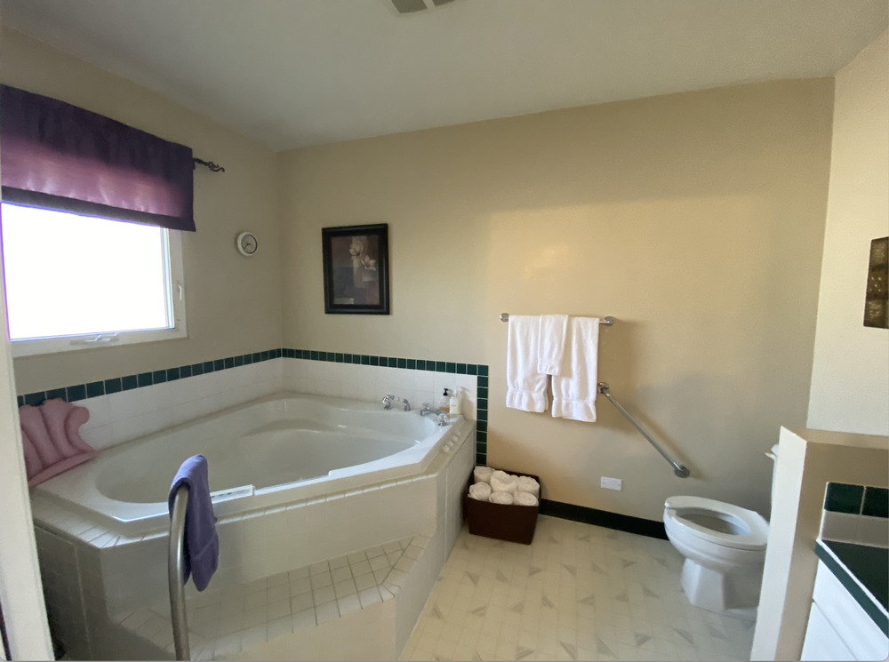 Bathroom with a corner bathtub, window, towels, toilet, and green tile accents