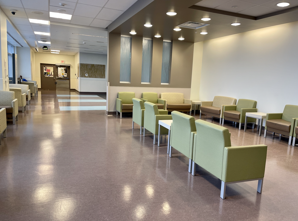 Quiet waiting area with green chairs, small tables, polished floor, ceiling lights, and an EXIT sign.