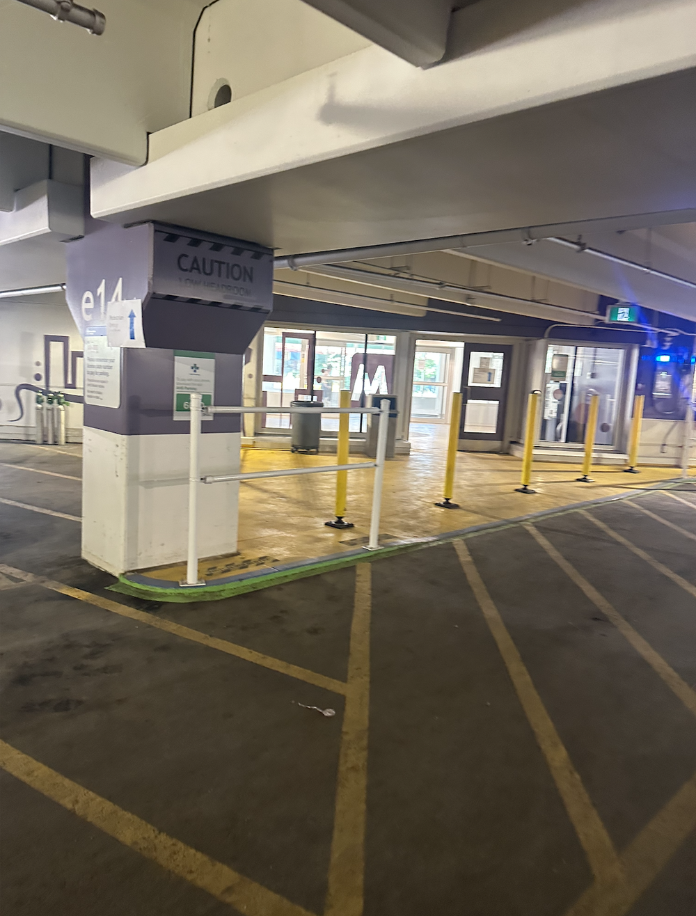 Parking garage entrance area with caution sign, yellow posts, glass doors, and an emergency exit sign