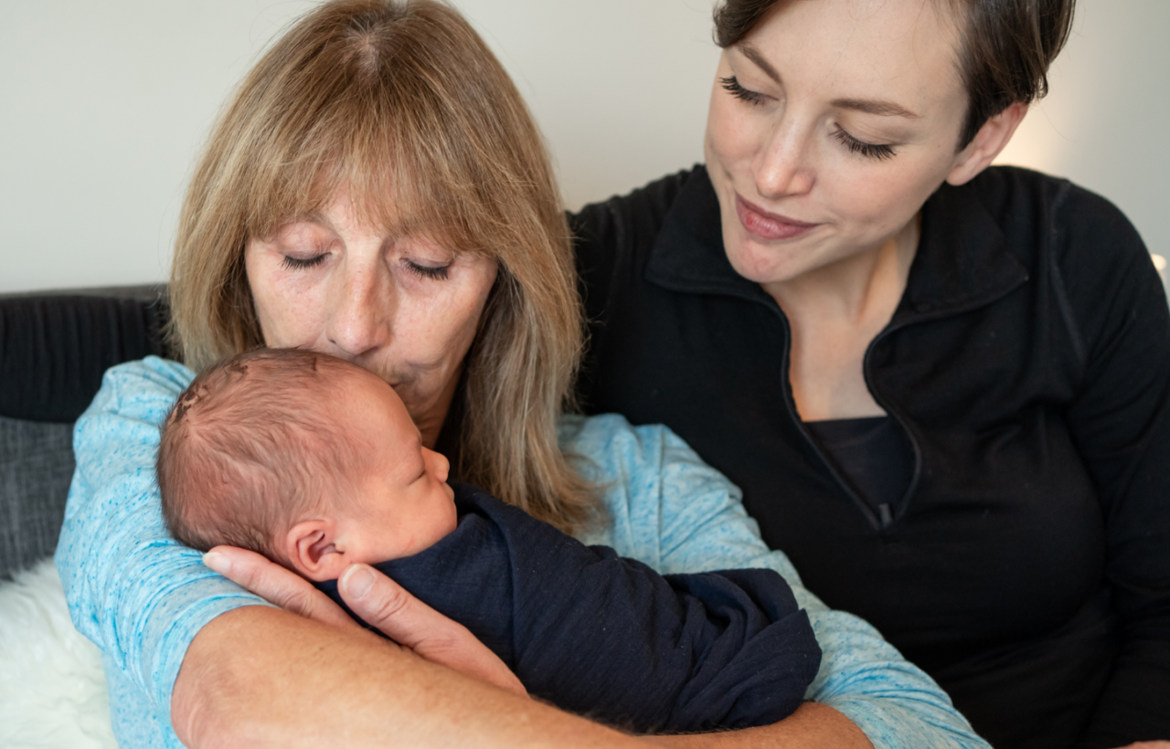 Older woman holding and kissing a sleeping newborn while another woman sits close beside them