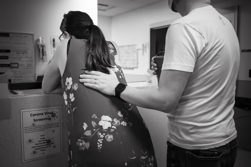 Person in a floral dress leans at a counter while another person rests a hand on their back.