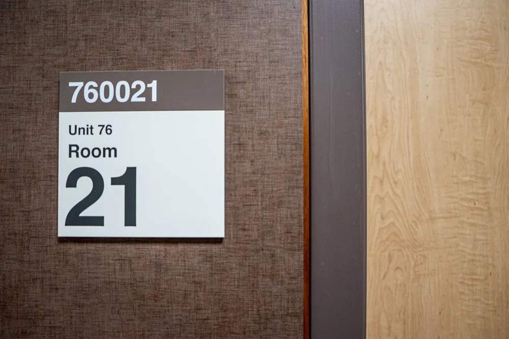 Sign reading 760021, Unit 76, Room 21 beside a wood-paneled doorway.