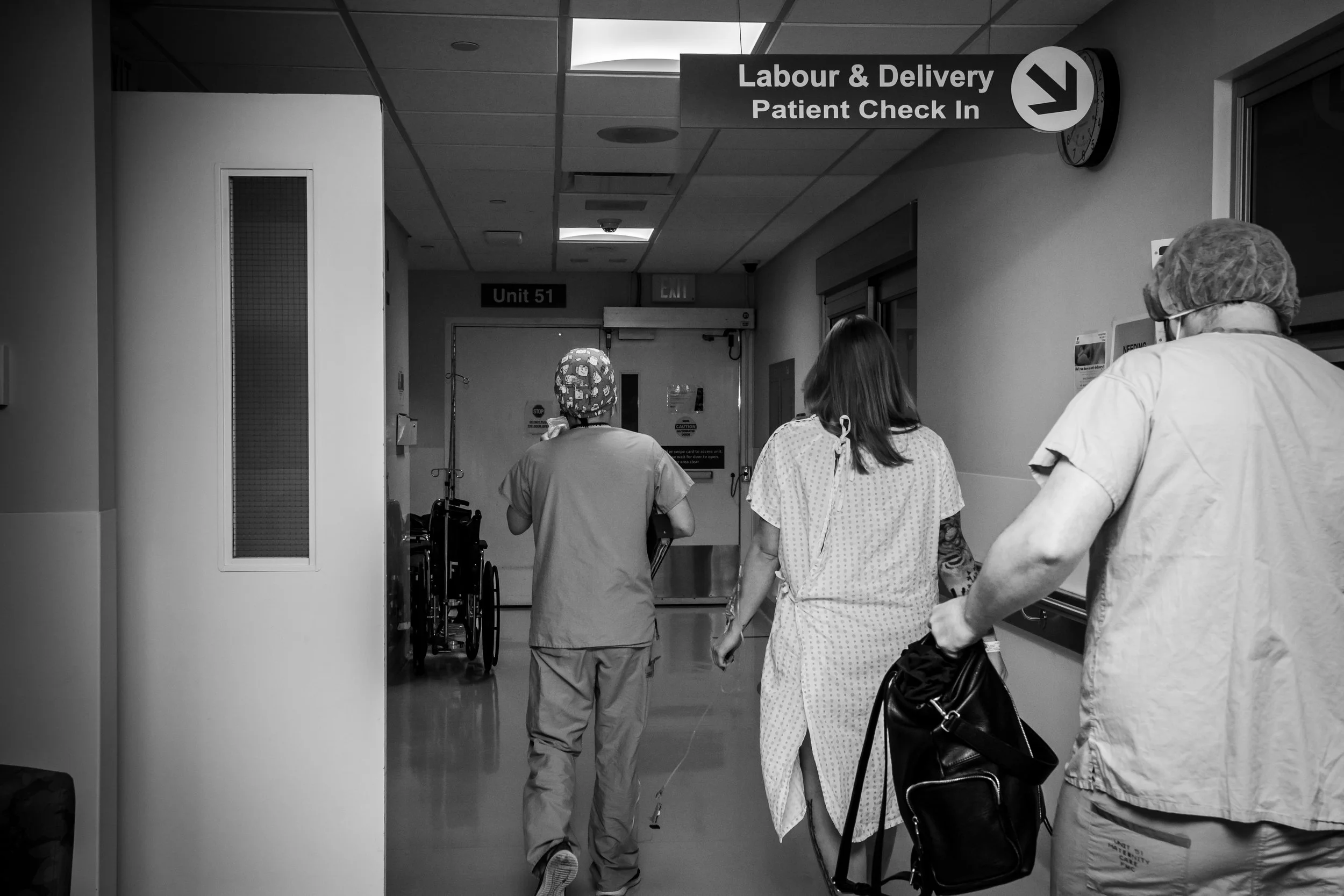 People walk down a hospital corridor beneath a Labour & Delivery Patient Check In sign.