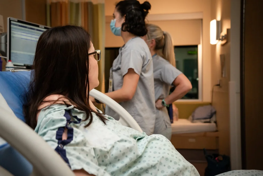 Patient in a hospital bed with two medical staff standing nearby in a clinical room.