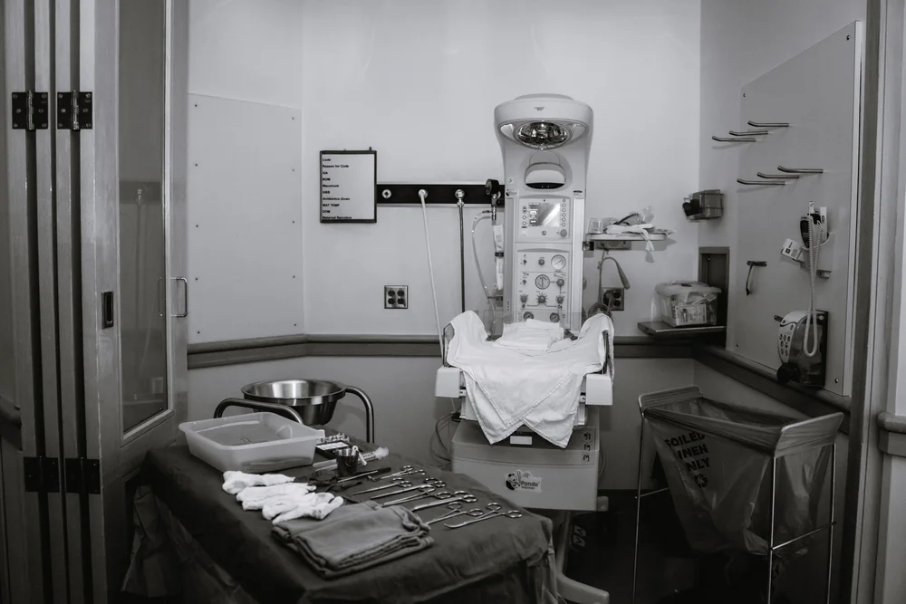 Hospital room with infant warmer, medical tools, folded linens, and a soiled linen bin