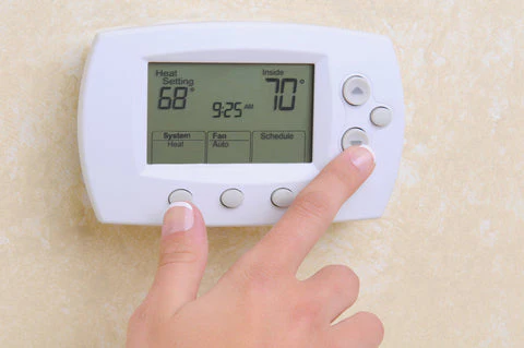 Hand pressing buttons on a wall thermostat showing heat settings around 68 and 70 degrees