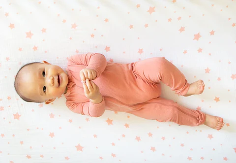 Baby in a pink sleeper lying on a white blanket with small pink stars.