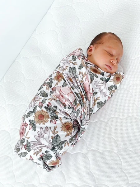 Sleeping infant swaddled in a floral blanket on a white textured mattress
