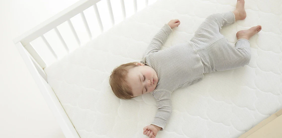 Sleeping baby in a striped outfit lying on a white crib mattress