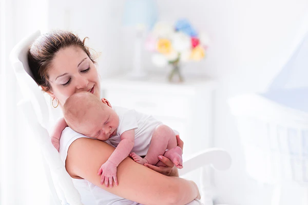 Woman cradling a sleeping baby in a bright, softly lit nursery room