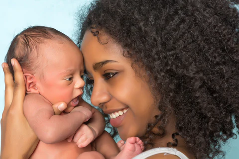 Smiling woman holding a newborn baby close to her face against a light blue background