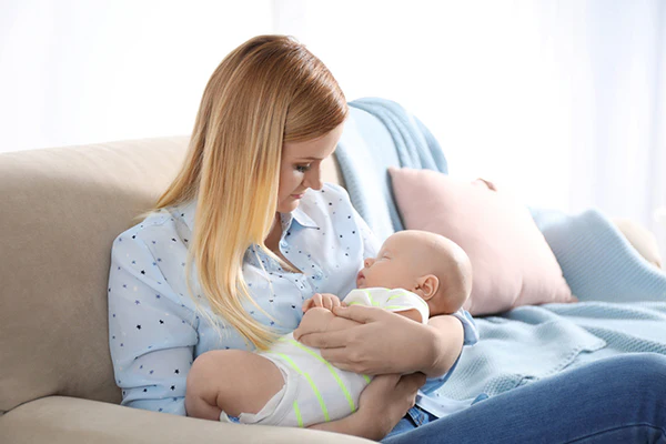 Woman sitting on a couch and holding a baby in her arms while looking down at the baby