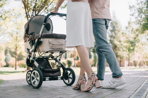 Two adults standing beside a stroller on a sunlit paved path outdoors.