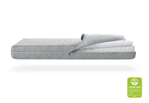 Gray crib mattress shown in side view with the top cover peeled back and a green GREENGUARD GOLD badge.