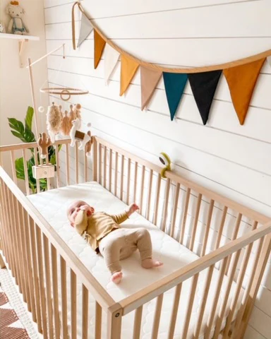 Baby lying on their back in a wooden crib in a bright nursery