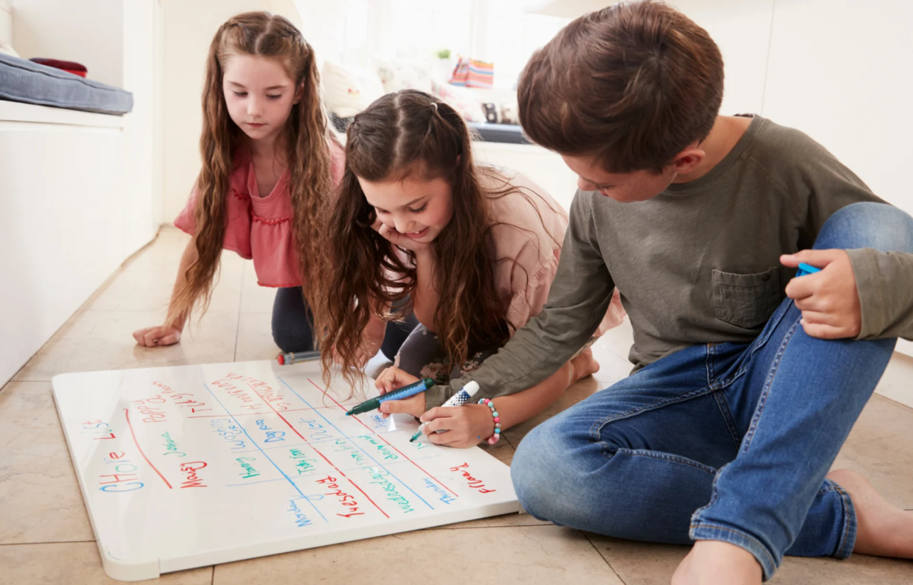 Three children writing on a whiteboard labeled Chore List on the floor