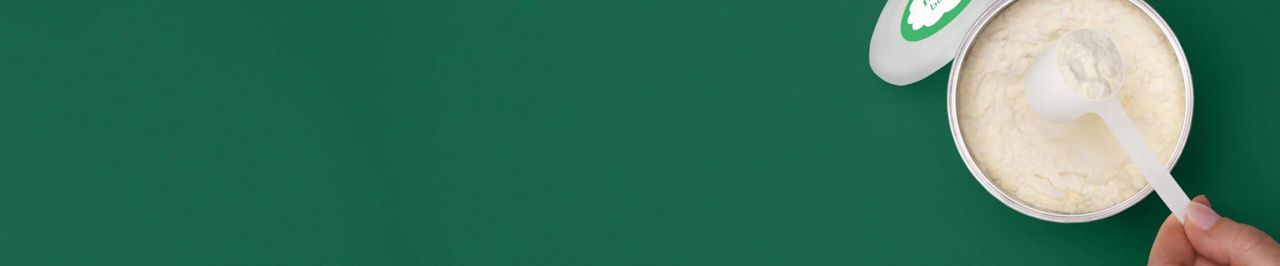 Open can of powdered formula with a scoop on a green background