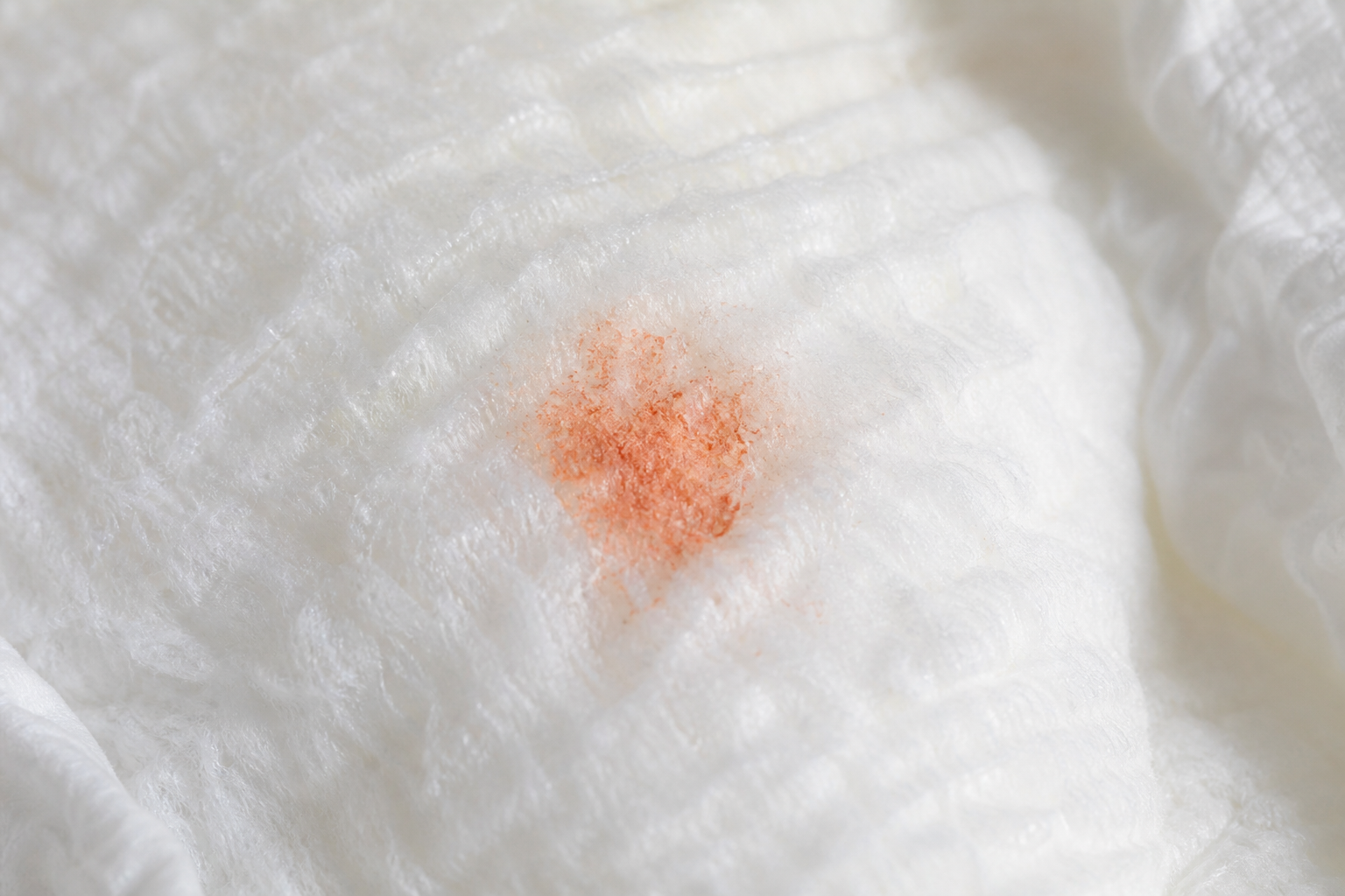 Close-up of a white diaper lining with a small patch of dry orange-pink crystalline residue.