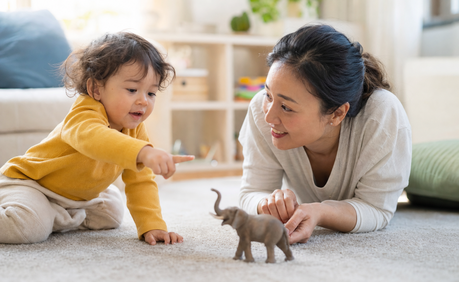 A toddler points to a toy animal while a caregiver watches and responds during floor play.